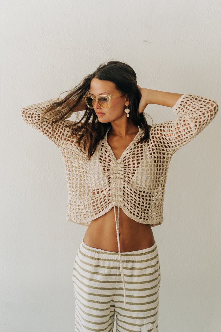 Woman wearing a crochet top and striped pants against a plain background