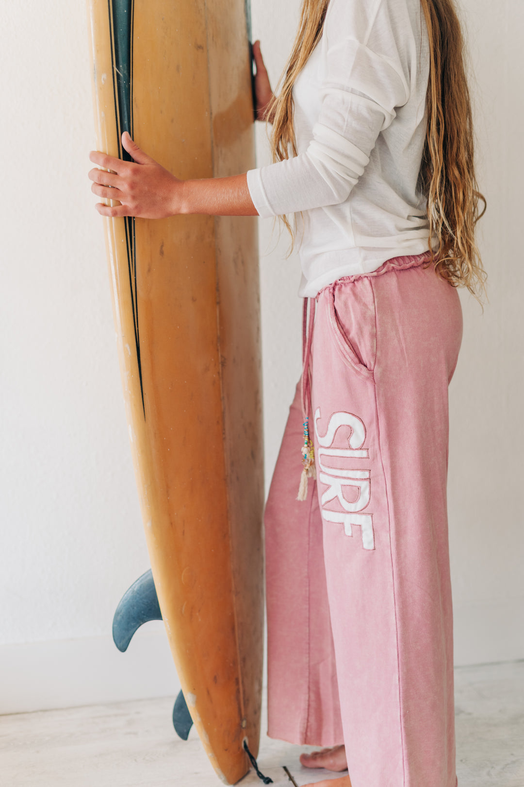 A woman in a white long-sleeve top and dusty pink drawstring pants with &