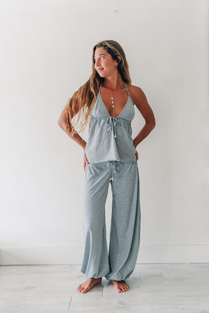 A woman modeling a light gray two-piece loungewear set consisting of a halter crop top and matching wide-leg pants, standing against a white wall.