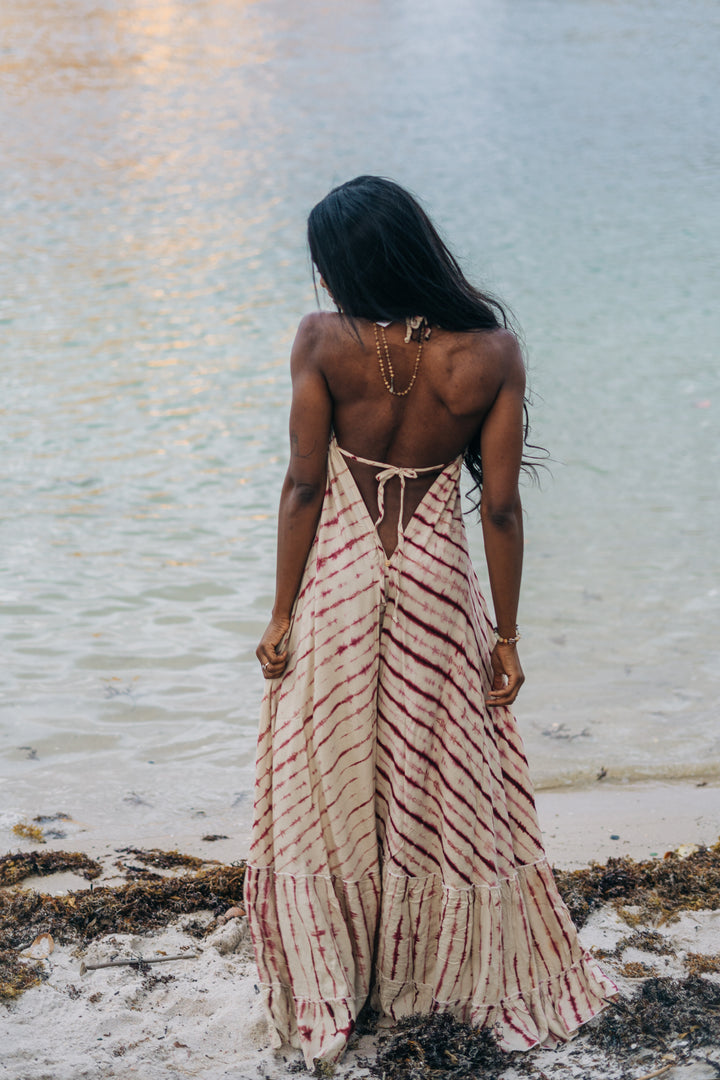 Woman in a long, patterned dress standing on a beach with water in the background