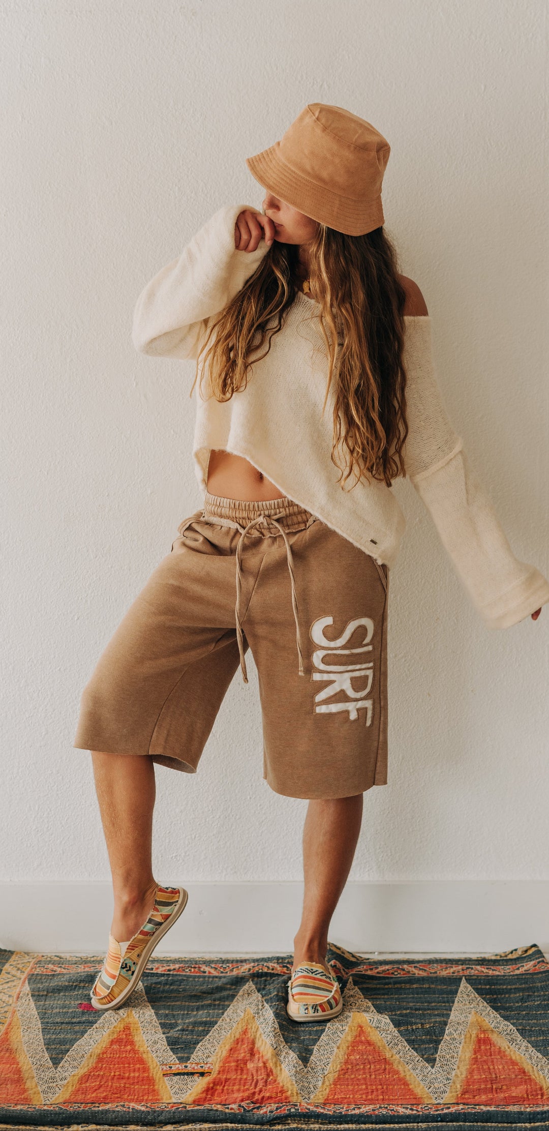 A woman modeling a bohemian-style outfit featuring tan drawstring shorts with &