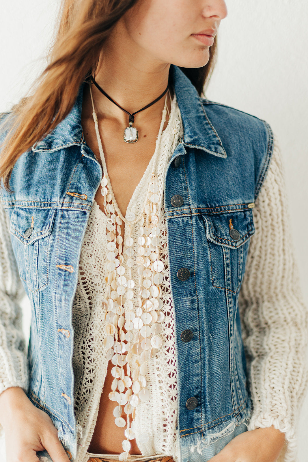 Woman wearing a denim vest over a white lace top with a neutral background