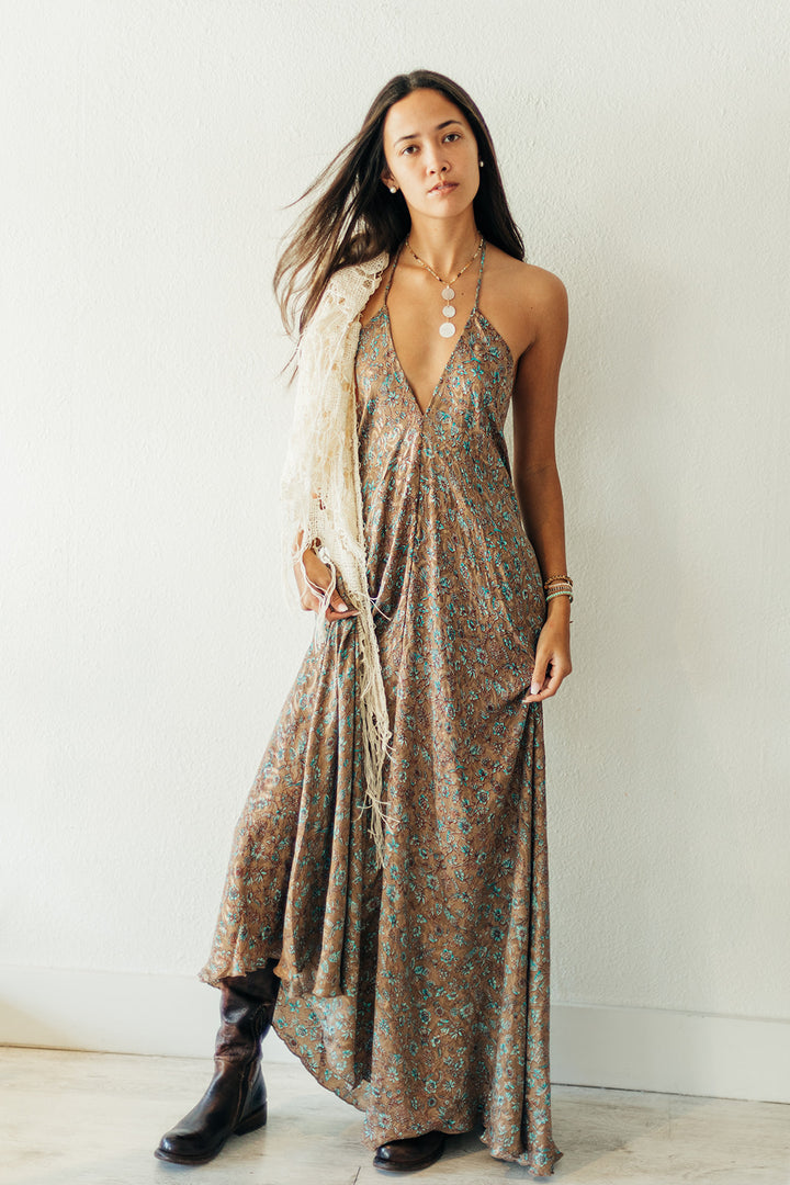 Woman wearing a patterned dress with a white scarf, standing against a plain background