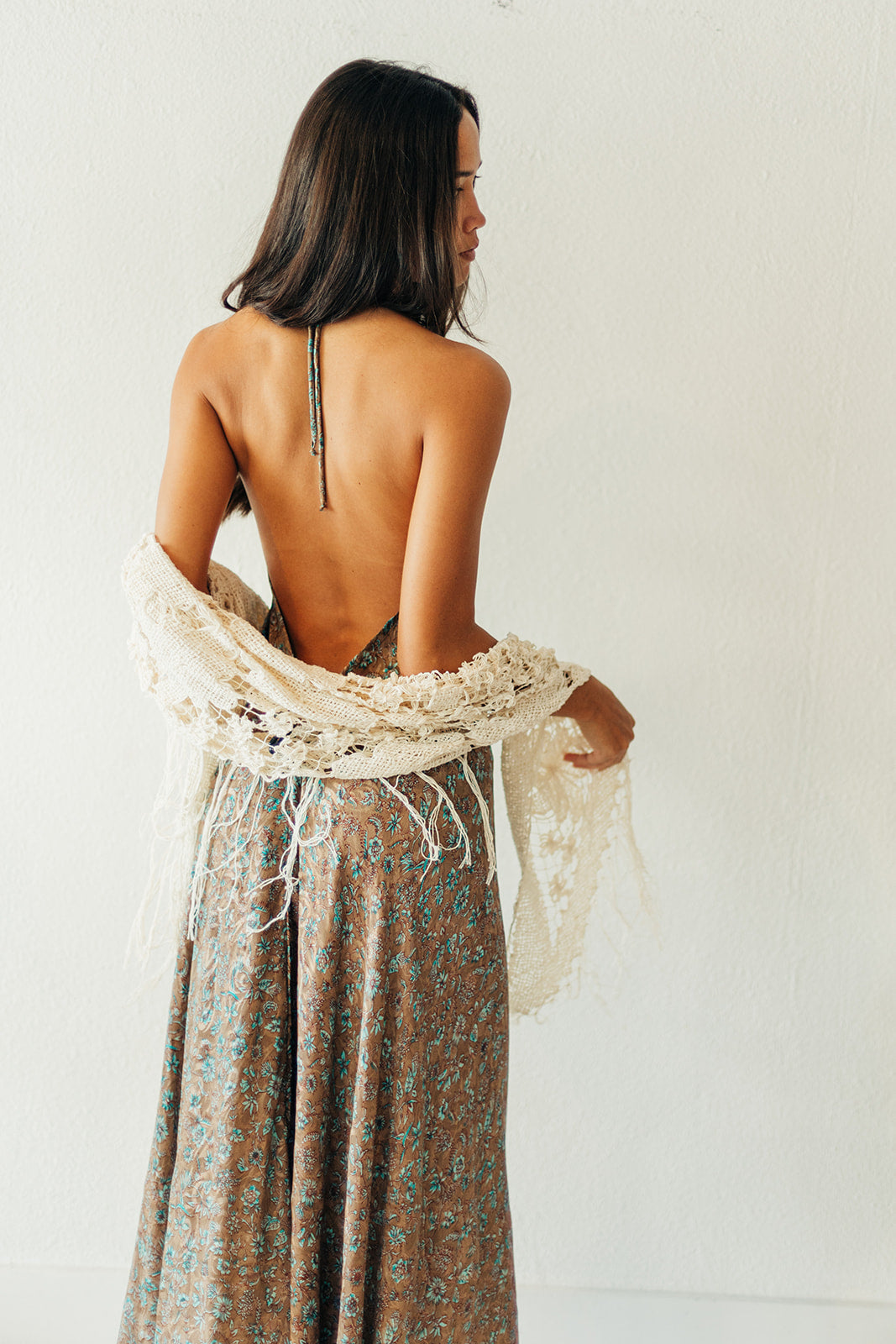 Woman wearing a floral dress with a backless design and a white shawl, standing against a plain background.
