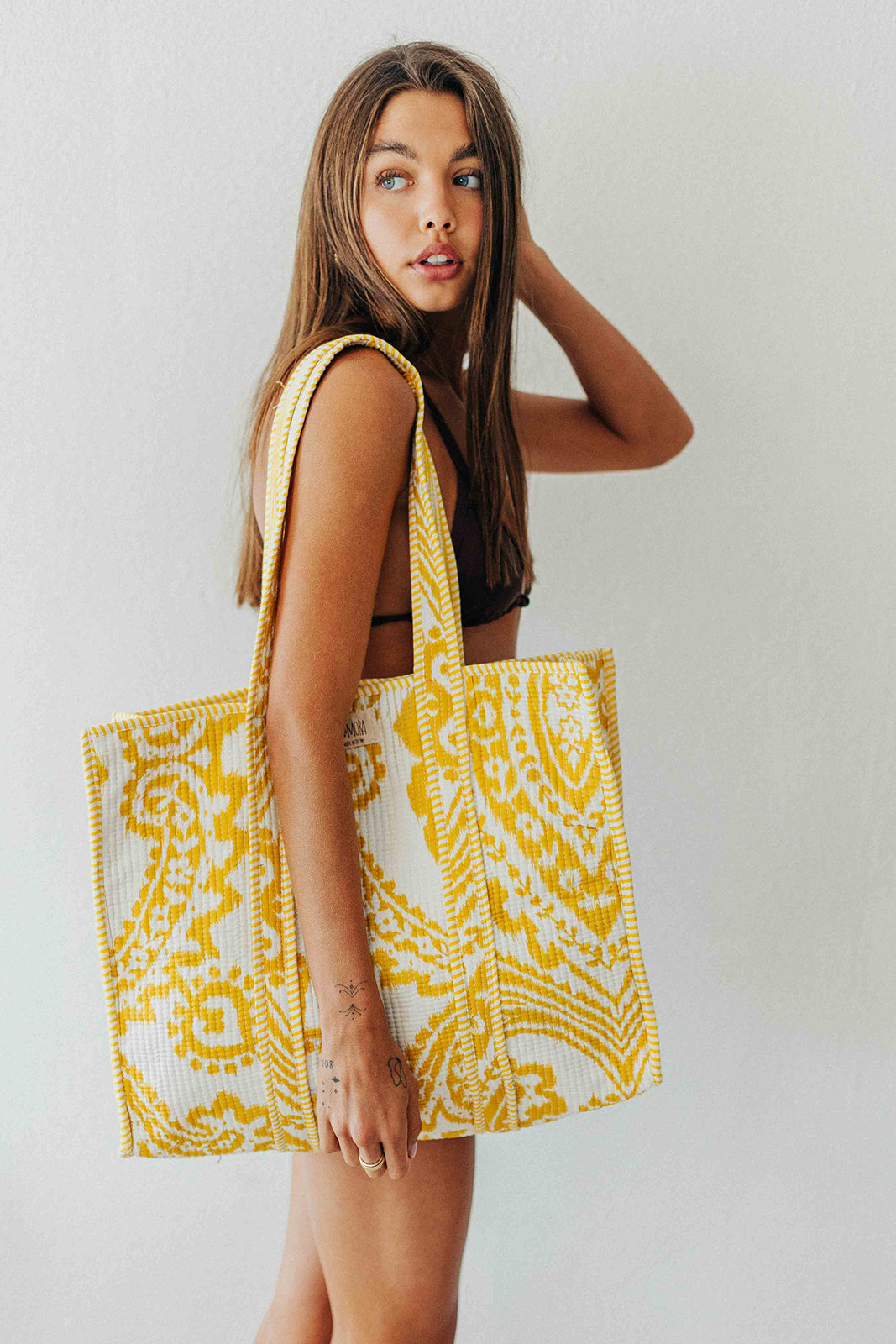 Woman holding a yellow and white patterned tote bag against a plain background